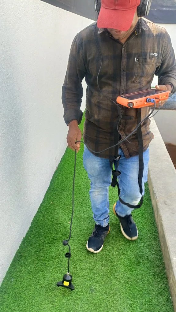 Laxman Enterprises technician wearing headphones and walking a Mumbai terrace with an orange acoustic leak-detection unit and ground probe